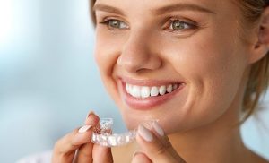 woman holding her Invisalign braces in hand ready to place into top teeth